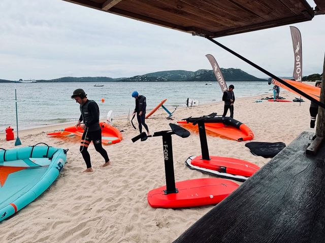 Moniteur et élèves préparant les planches et les ailes de wingfoil sur la plage, devant l'école